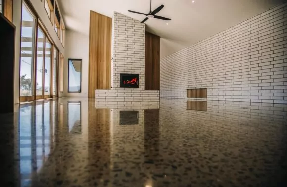 Modern living room featuring a white brick fireplace, polished terrazzo floor, wooden accents, and large windows inviting natural light