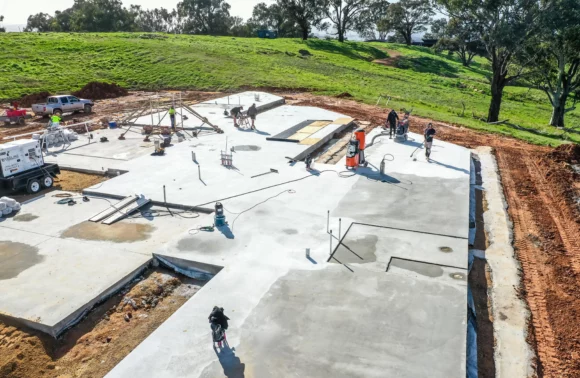 Workers are finishing a large concrete foundation for a construction project, with equipment and materials scattered around the site